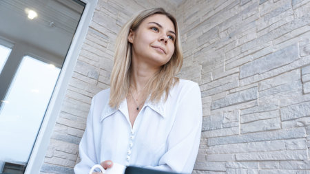 Side view. Young business woman with a cup of coffee sitting and taking notes in notebook. Student...