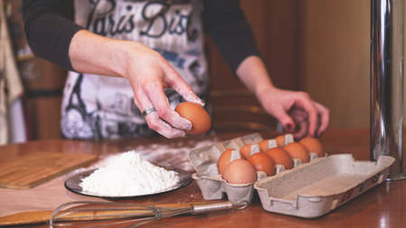 The hands of a female chef picking an egg for making dough while making bread with a pile of wheat nearbyの写真素材