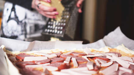 Closeup hand of chef baker making homemade pizza. Female hands rubbing cheese on pizzaの写真素材