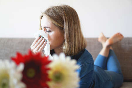 Spring cold or allergies. A young attractive girl is allergic to flowers, uses a napkin at homeの写真素材