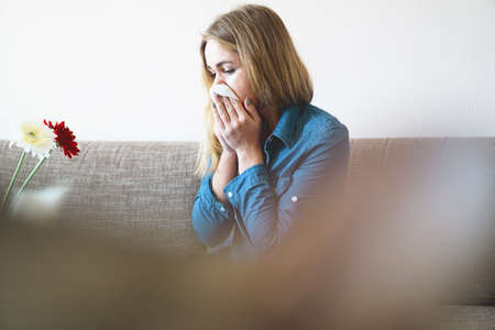 Spring cold or allergies. A young attractive girl is allergic to flowers, uses a napkin at homeの写真素材