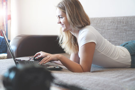 Young woman relaxing with a laptop in her living room - side viewの写真素材