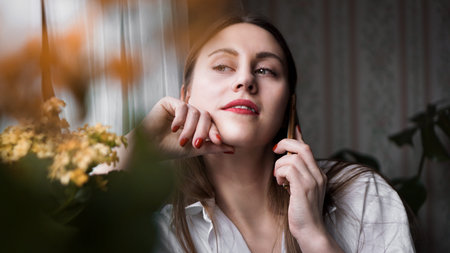 Pretty woman with red lips talking on phone near window at home in morning sunlight