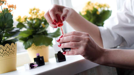 Pair of female hands opening nail polish bottle. Nail polishes on the bright window-sill with flowersの写真素材