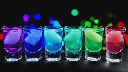 Variation of hard alcoholic shots with ice served on bar counter. Blur neon backgroundの写真素材