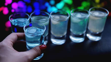 Female hand with a shot of alcohol, neon blurred background in barの写真素材