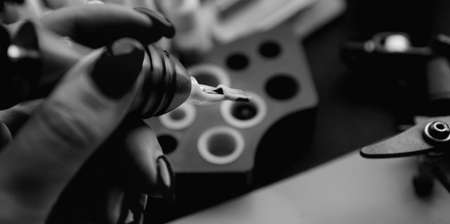 Female hand holding tattoo machine. Hand without gloves - practice and training tattoo. Dark background - black and white photoの写真素材