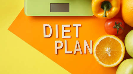 Concept diet. Healthy food, kitchen weight scale. Vegetables and fruits lettering Diet plan on orange backgroundの写真素材