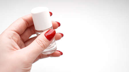 Girl with red nails holds clear polish or cuticle oil on white background. Health and nail careの写真素材
