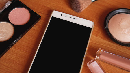 Smartphone with empty screen and cosmetics on light wooden background. Top view, flat lay. Mobile...