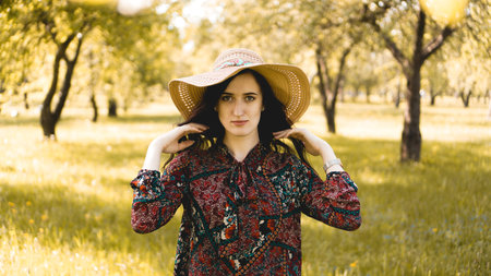 Summer portrait, beautiful young woman wearing straw hat at sunset time on the garden