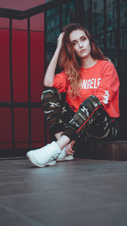 Fashion model wearing red hoodie with the inscription los angeles posing in the city at parking....