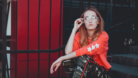 Fashion model wearing red hoodie with the inscription los angeles posing in the city at parking....