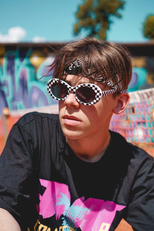 Portrait of a young man with sunglasses relaxing against graffiti background outdoors