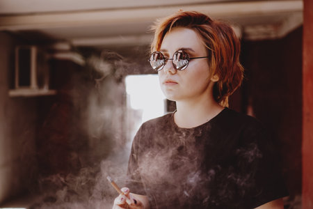 Millennial cool pretty girl with short red hair and mirror sunglasses smoking cigarette in the old...