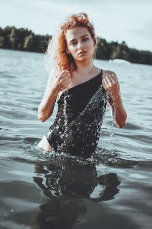 Young beautiful woman standing in the water. Black swimsuit. Vintage style. vertical photoの写真素材