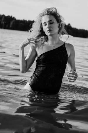 Young beautiful woman standing in the water. Black swimsuit. Vintage style. vertical photo. Black and whiteの写真素材