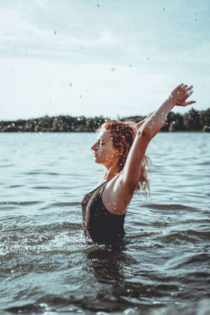 Young beautiful woman standing in the water. Black swimsuit. Vintage style. vertical photoの写真素材