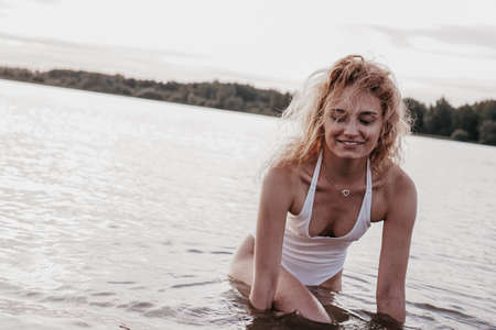 Beautiful sexy woman in a white swimsuit with an open back posing near the lake, photo in vintage styleの写真素材