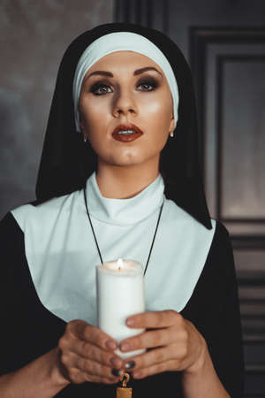 Young catholic nun is holding candle in her hands. Photo on black background. Portrait of beautiful womanの写真素材