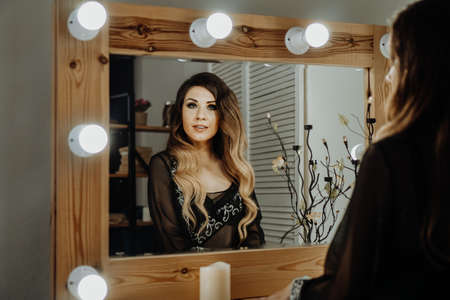 Beautiful young woman looking at her reflection in a dressing room mirror. Happy glamorous womanの写真素材