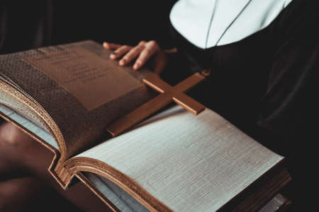 Nun in religion black suit holds Bible and posing on camera with big book on a black background. Close-up. Religion concept.の写真素材