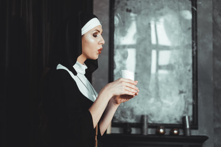 Young catholic nun is holding candle in her hands. Photo on black background. Side view.