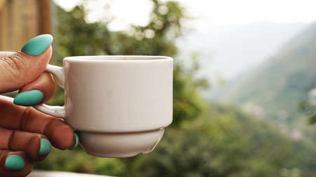 Hand white cup of hot coffee. In the morning, cold mountain views, soft focus, blurredの写真素材
