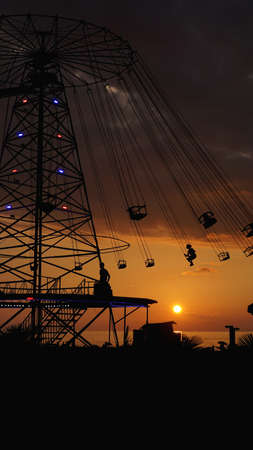 Swinging carousel roundabout chain ride at sunset. Entertainment on the beach, silhouettes of palm trees on a background of sea sunsetの写真素材