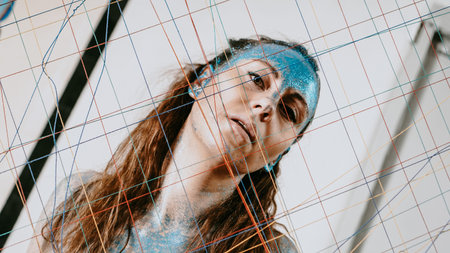 Brunette girl behind the threads net. Portrait of beautiful woman with blue sparkles on her face....