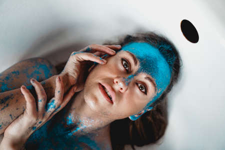 Portrait of beautiful woman with blue sparkles on her face in the bath. The concept of Individualityの写真素材