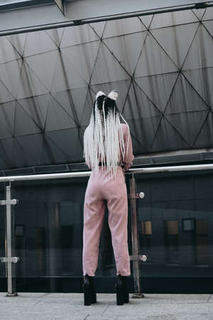 Young woman with futuristic looks. Girl with black and white pigtails standing with her back. Against the background of a futuristic buildingの写真素材