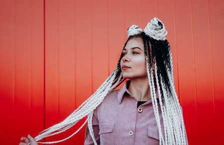 Portrait of beautiful cool girl with Senegalese pigtails and dreadlocks over red wallの写真素材