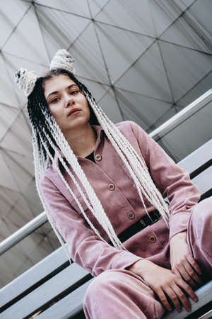 Young woman with futuristic looks. Girl with black and white dreadlocks or pigtails. Against the background of a futuristic buildingの写真素材