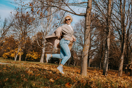 Beautiful woman in autumn park jumping and smiling - sunny day