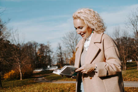 Woman in an autumn coat holds a book. Autumn park on a sunny dayの写真素材
