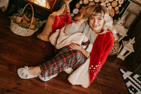 A beautiful young woman in a red plaid sits in a warm classic New Year interiorの写真素材
