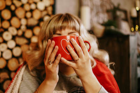 Young woman in plaid with cup of hot tea in a Christmas cozy interior. The concept of preparation for the holidays, Make a wish and dreamの写真素材