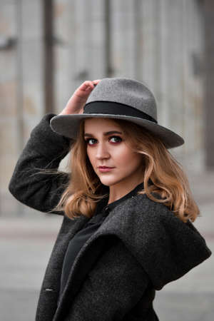 Portrait of beautiful woman with blond hair wearing hat and gray coat. Outdoor portrait in cityの写真素材