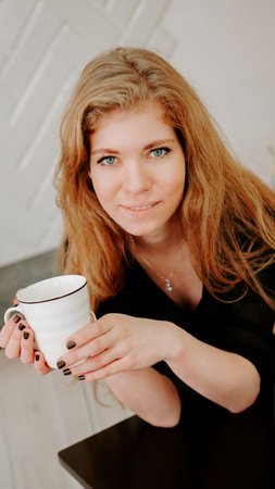 Woman holds a cup of coffee in the morning in Christmas kitchen. Happy young woman having fun and...