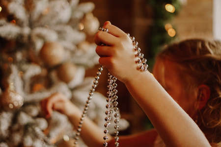 Girl decorates the christmas tree with beads. Selective focus on a small children handの写真素材