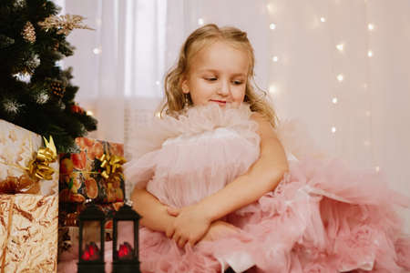 Girl in a pink dress near the Christmas tree and boxes with giftsの写真素材