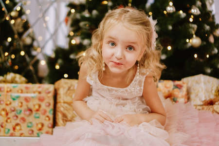 Cute little girl in pink dress with present on background Christmas tree. Merry Christmas and Happy New Year and Holidaysの写真素材
