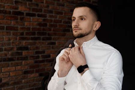 Close-up handsome and successful man in an expensive suit. He is in a white shirt. The man straightens his collarの写真素材