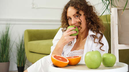 Young woman eating green apple at home. Healthy nutrition, diet food concept. Close-up portrait of beautiful young woman eating organic green apple.の写真素材
