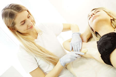 Waxing woman armpit with spatula. Salon wax beautician epilation procedure. Waxing female body for hair removal by therapist close upの写真素材