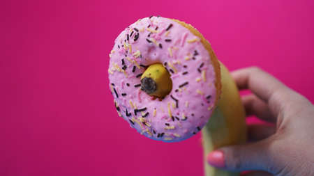 Sweet donut and banana in hand on pink color background. Sex and Erotic conceptの写真素材