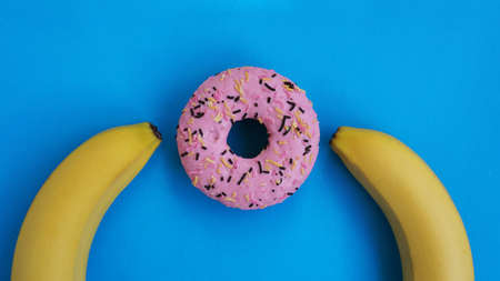 Two bananas and a pink donut on a blue background. Erotic concept and group sexの写真素材