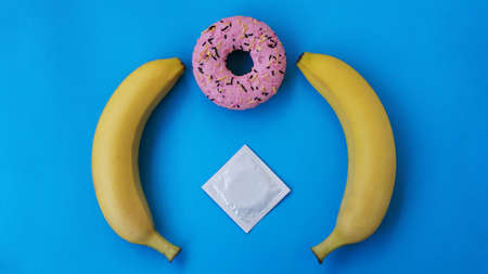 Two bananas and a pink donut on a blue background. Erotic concept and group sex. Condom and protected sexの写真素材