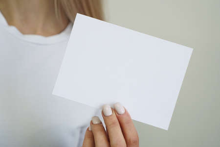 Woman in white t-shirt hold white blank paper sheet in hand - mockupの写真素材